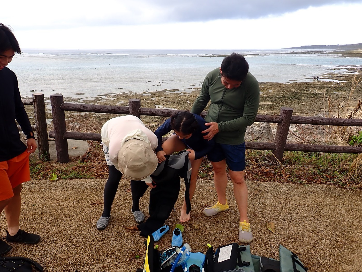 天然水族感の海岸沿いの柵の前でガイドがシュノーケル器材の装着を手伝う様子。天然水族館での自然体験シュノーケル