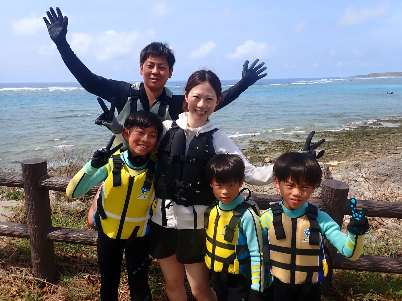 天然水族感の参加者が青空と海岸を背景に並んで立つ。天然水族館での自然体験シュノーケルを楽しむ準備中