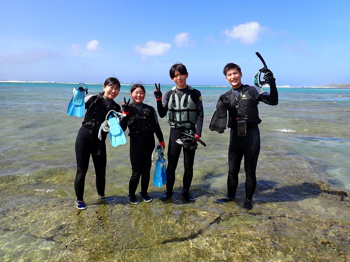 浅瀬の岩場でライフジャケットとフィンを着用し笑顔で集合する参加者たち