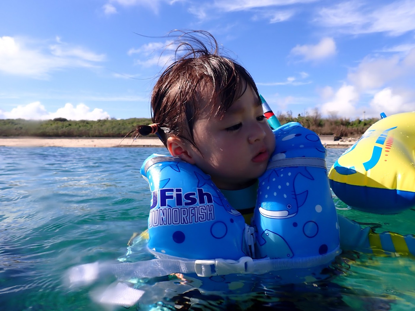 浅瀬で水に体を預け、フロートにつかまり水慣れをしている子供