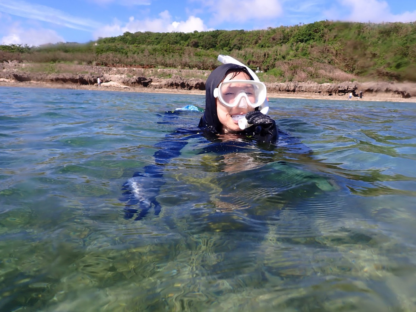 海中で笑顔でカメラを見ている参加者と、遠くに見える海岸線