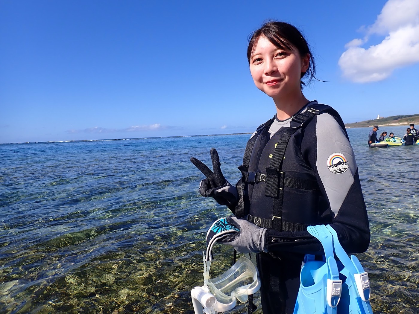 浅瀬に立ちピースサインをする参加者と天然水族感のあるリーフの海岸風景