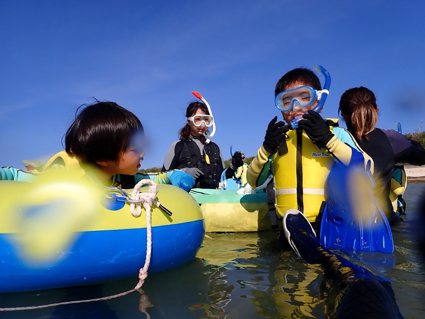 天然水族感。青い空と海、水面近くでシュノーケル器材を身につけ練習する子供たちと担当の池田